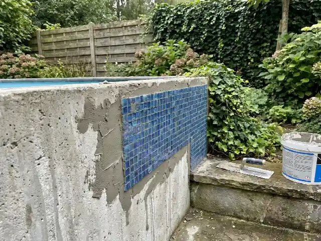 Betonnen zwembadwand die met blauw glasmozaïek wordt afgewerkt